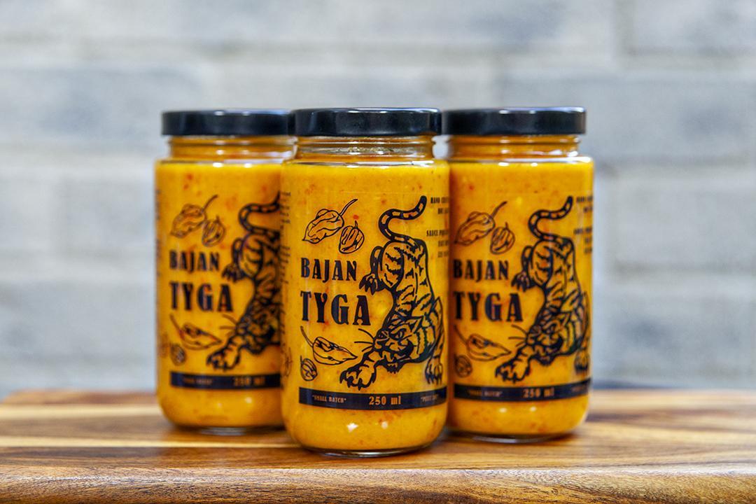Three glass jars of Bajan Tyga micro batch hot sauce.