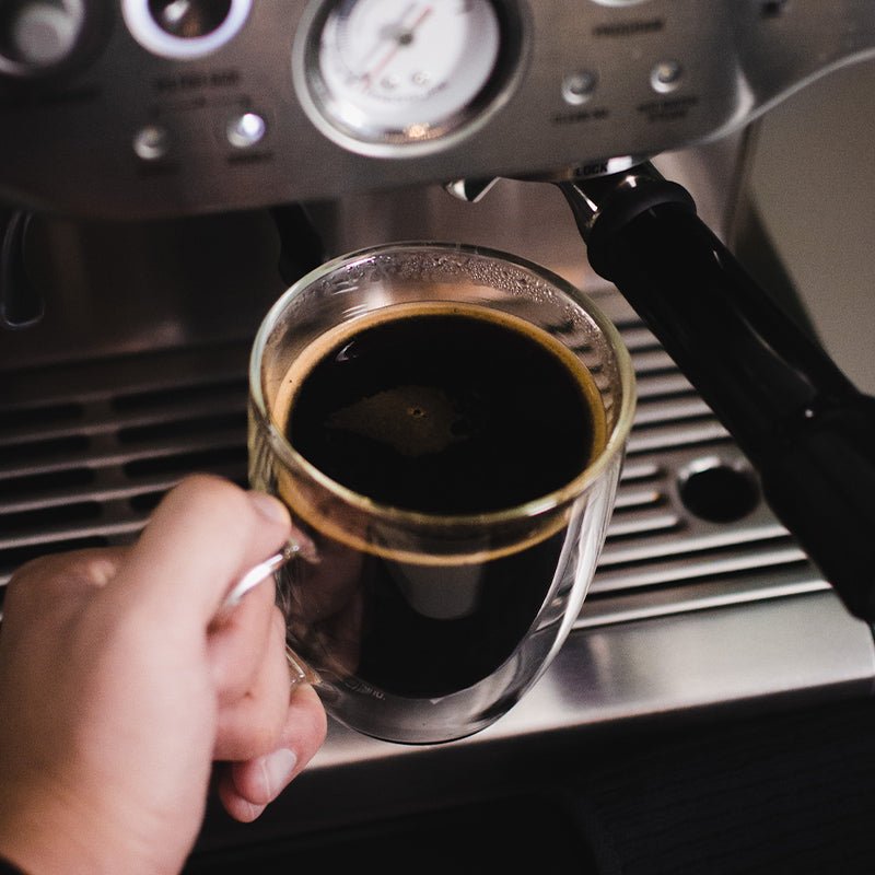 Glass of hot espresso and water in front of espresso machine.