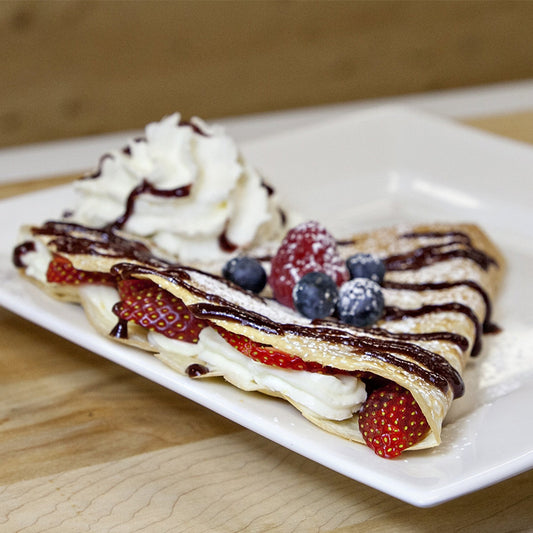 A crêpe filled with cream cheese, strawberries and whipped cream, topped with blueberries, whipped cream and chocolate drizzle.