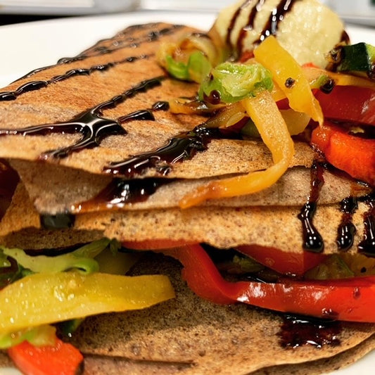Vegan buckwheat crepe with bell peppers, brussels sprouts, onions, zucchini, hummus and balsamic glaze.