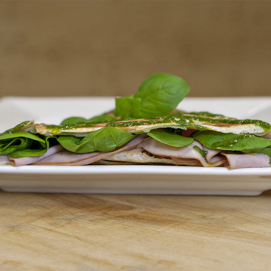 Crêpe filled with black forest ham, Swiss cheese, and greens, topped with pesto drizzle and basil leaves.