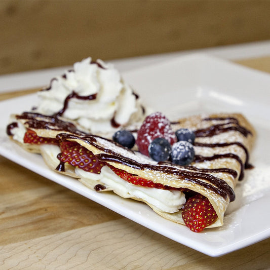 A crêpe filled with cream cheese, strawberries and whipped cream, topped with blueberries, whipped cream and chocolate drizzle. 