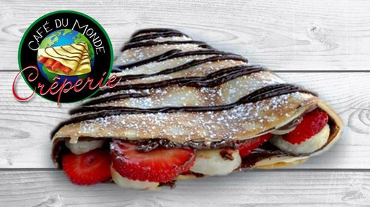 Crêpe filled with Nutella, strawberries, and bananas, topped with icing sugar and chocolate drizzle.
