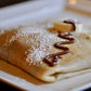 Folded crêpe with icing sugar and Nutella on top.