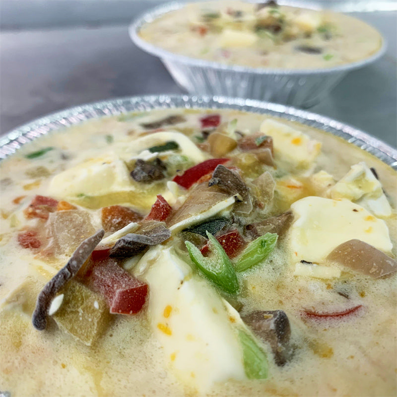 Frozen quiche with various vegetables and cheeses in aluminum tray.