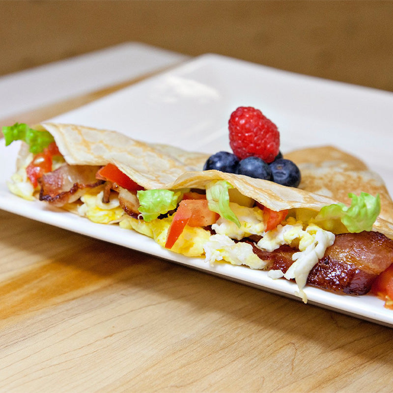 A crêpe filled with eggs, bacon, lettuce and tomatoes and topped with blueberries and raspberries. 