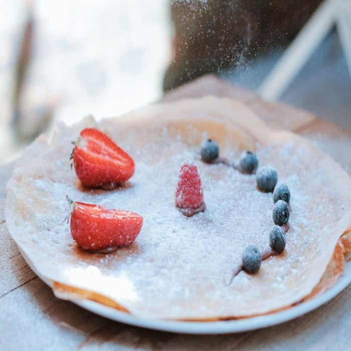 A delicious crepe you can design yourself. This is an image of an icing sugar coated crepe with fruit arranged in a smiley face.