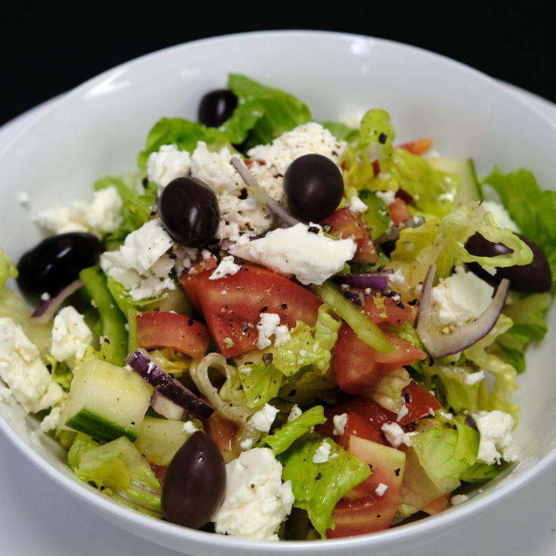Bowl of salad with fresh lettuce, green and black olives, feta cheese, cucumbers, tomatoes and homemade Greek dressing.