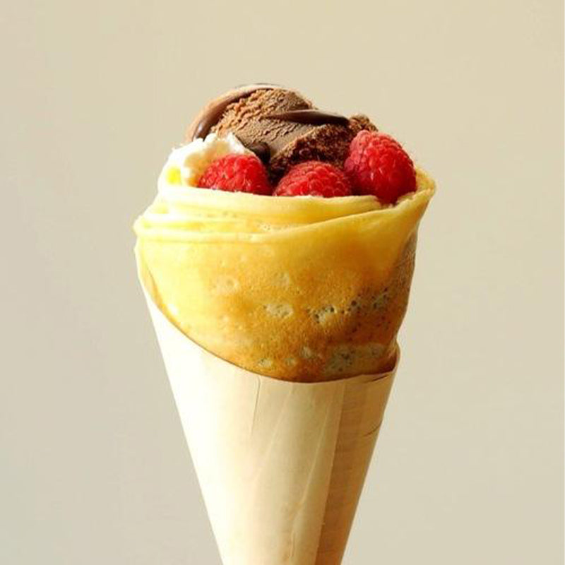 Crêpe rolled into an ice cream cone shape with chocolate ice cream and raspberries in the top. 