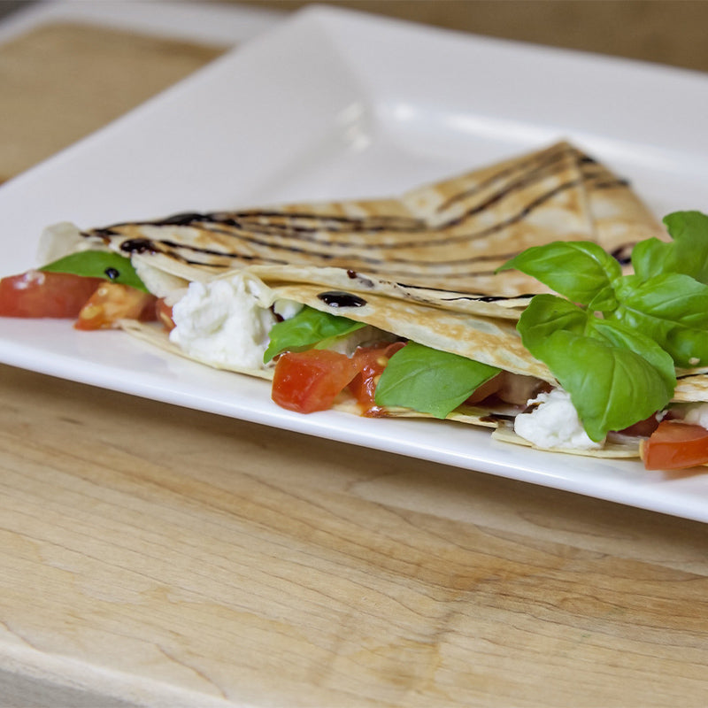 A plated crêpe with goat cheese, tomatoes and basil inside and basil and balsamic glaze on top.